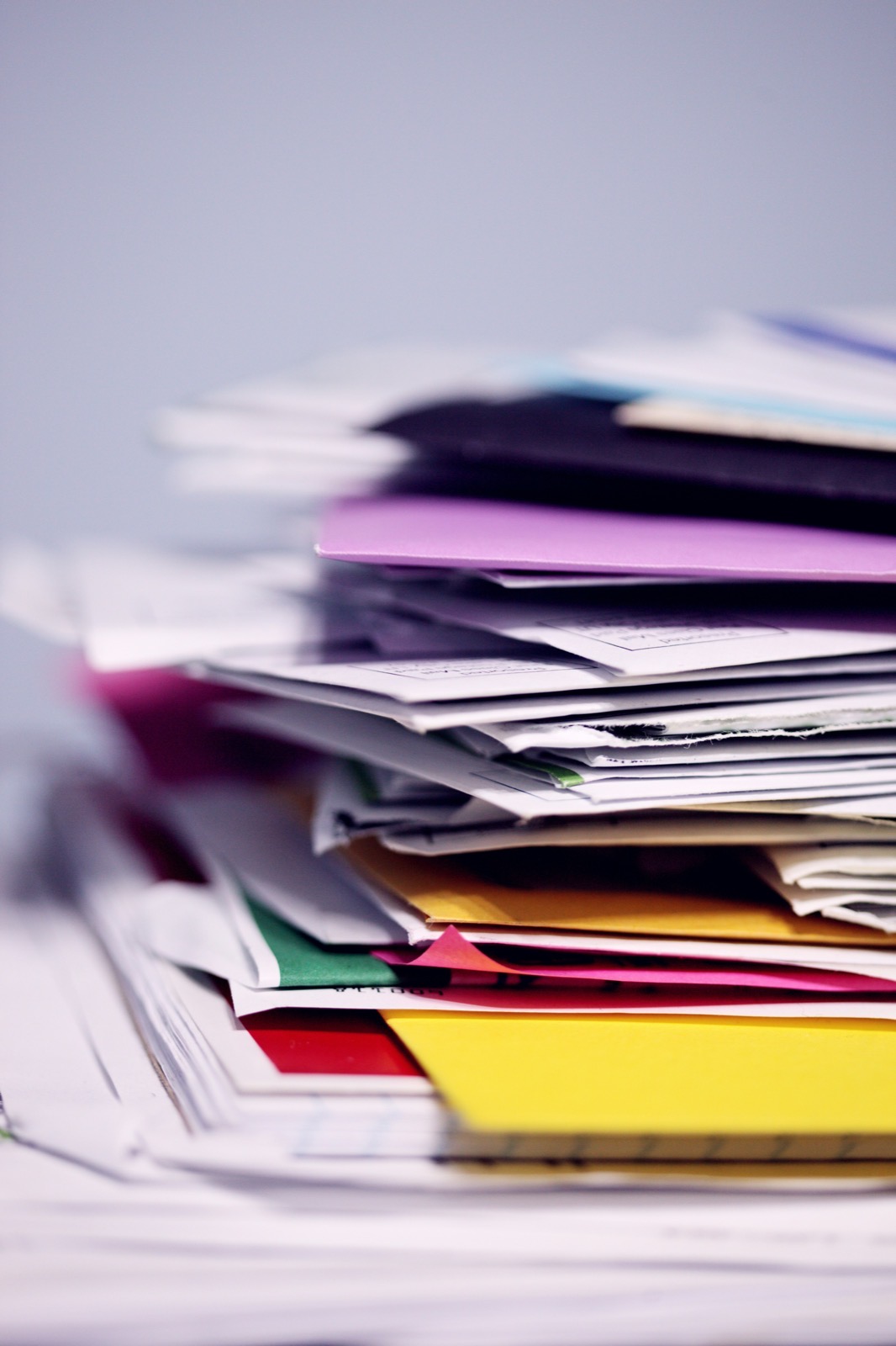 A tall stack of papers, envelopes, and colored folders